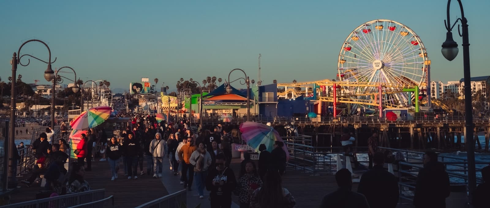 Crowded pier boardwalk with amusement rides and ferris wheel